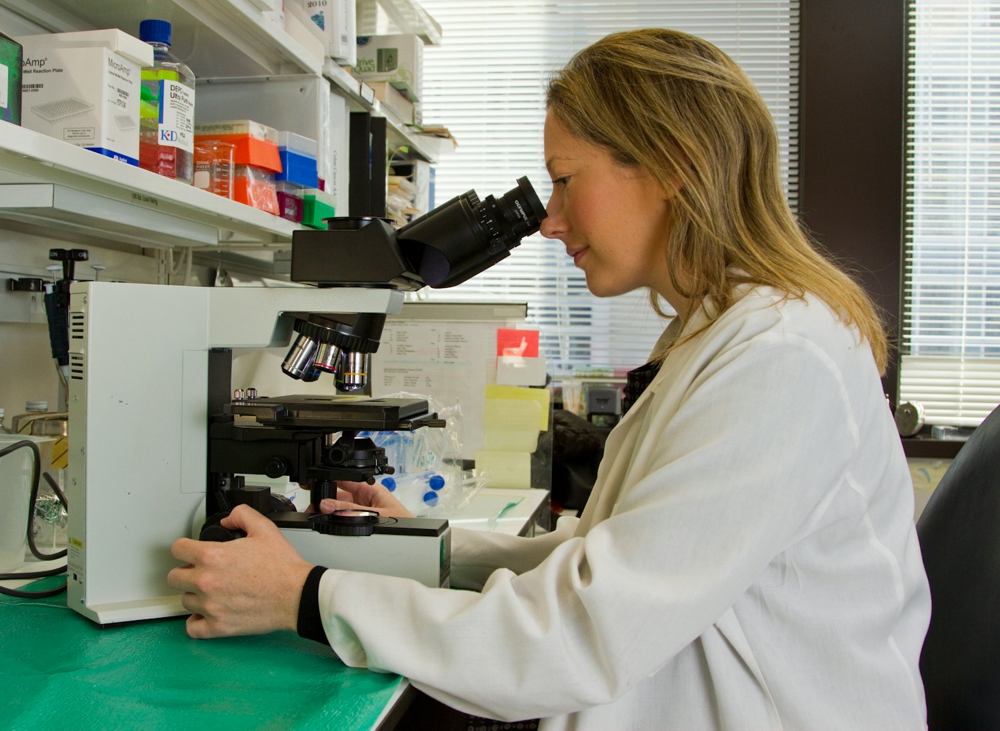 Mujer con bata de laboratorio examinando un microscopio.