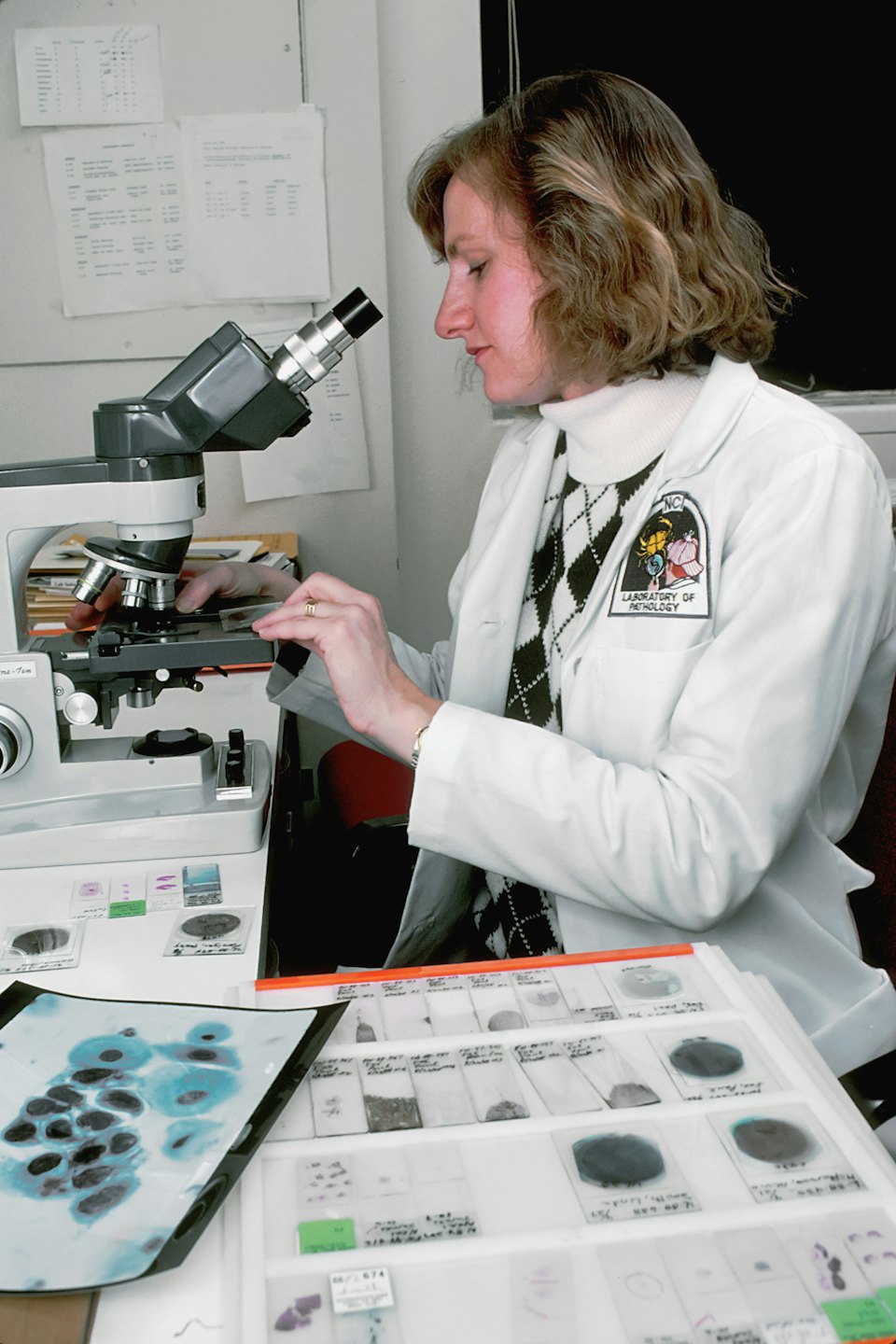 Mujer examina portaobjetos médicos con un microscopio en un laboratorio.
